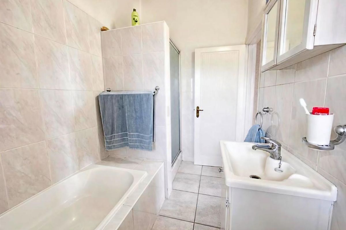 A functional bathroom featuring a built-in bathtub, separate shower enclosure, vanity basin, and wall-mounted storage cabinet with neutral tiled finishes throughout.