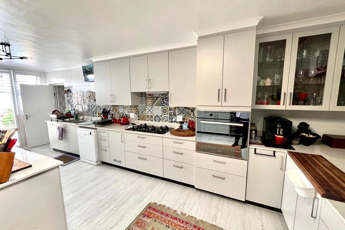 A well-appointed kitchen featuring white cabinetry, a gas hob, built-in oven, and decorative patterned tile backsplash with light wood-look flooring.