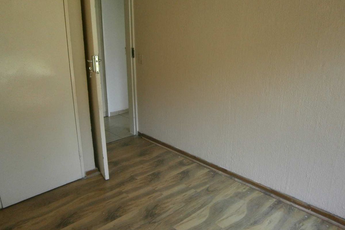 An empty bedroom featuring wood-look laminate flooring and neutral painted walls, with a doorway leading to an adjacent tiled space.