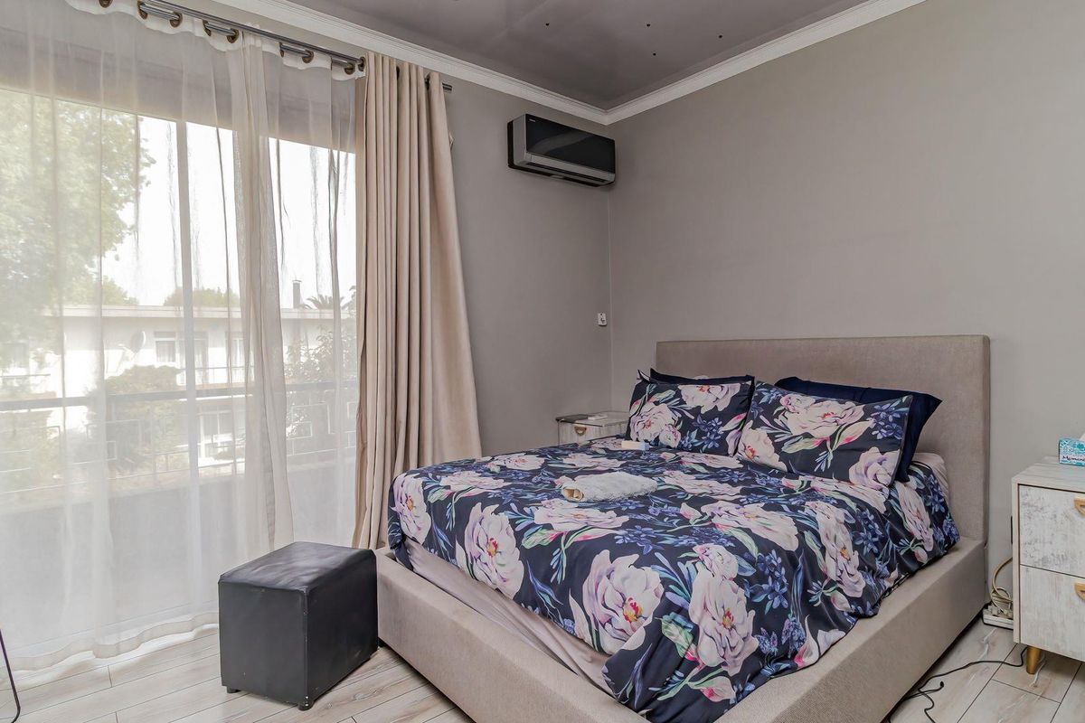 A well-maintained bedroom featuring laminate flooring, cove molding, and a wall-mounted split-system air conditioner with access to a balcony through sliding glass doors.