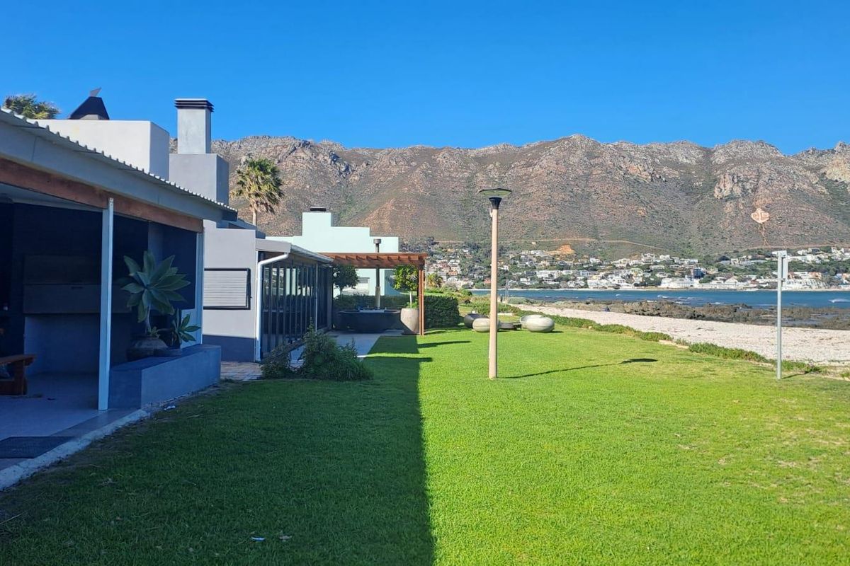 Rear exterior view of the townhouse featuring a covered patio with built-in braai, a well-maintained lawn, and scenic mountain and coastal views.