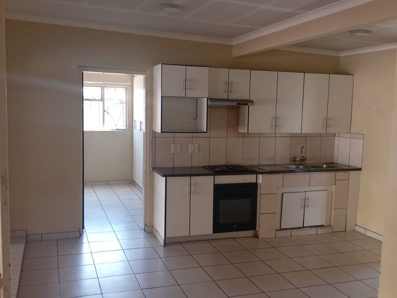 A functional kitchen featuring built-in cabinetry, an integrated oven and hob, tiled flooring, and a double sink, leading into a separate utility area.