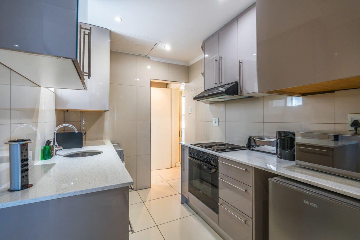 Modern kitchen featuring high-gloss cabinetry, stone countertops, integrated oven, hob, and extractor fan with tiled flooring and backsplash.