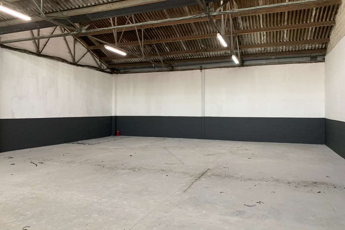Spacious industrial warehouse unit featuring high exposed truss ceilings, concrete flooring, and dual-tone painted masonry walls, suitable for storage or light manufacturing.
