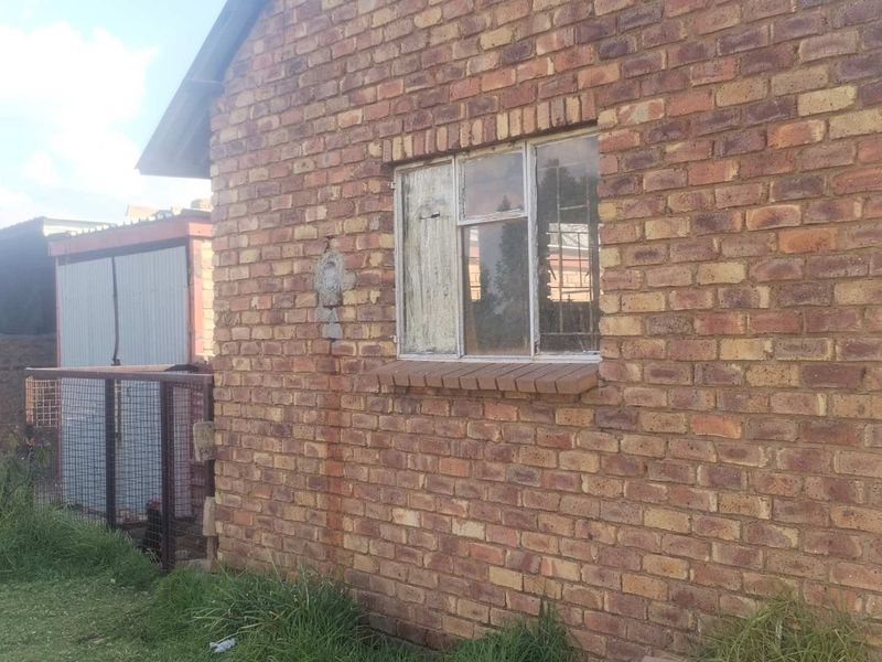 Exterior view of a face brick building featuring a weathered metal frame window and adjacent corrugated metal structure.