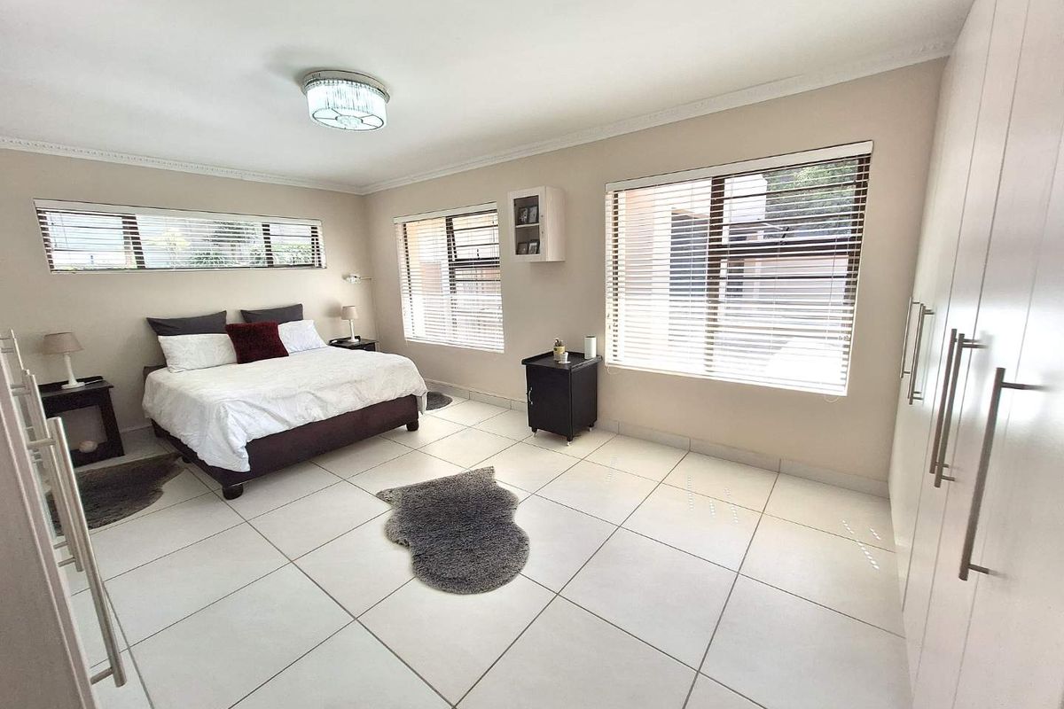 Spacious bedroom featuring large format floor tiles, built-in cupboards, and multiple windows with fitted blinds, offering a bright and neutral living space.