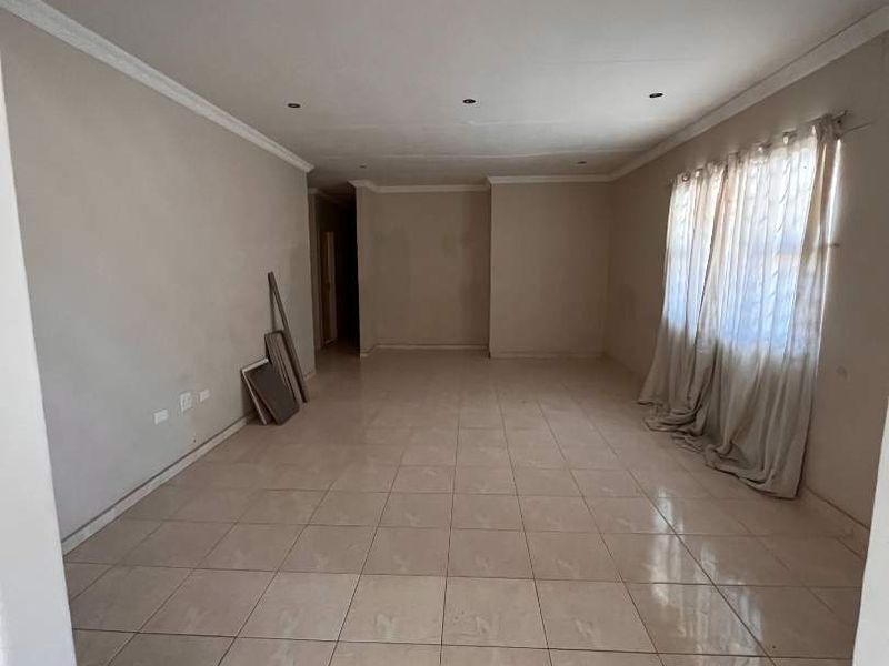 A spacious, empty living area featuring neutral tiled flooring, recessed ceiling lights, and decorative coving, providing a blank canvas for interior design.