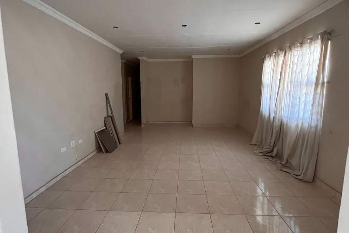 A spacious, empty living area featuring neutral tiled flooring, recessed ceiling lights, and decorative coving, providing a blank canvas for interior design.