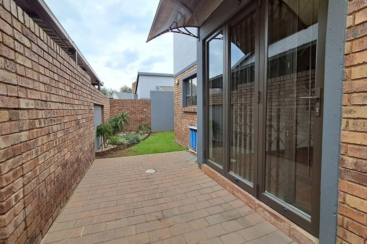 A paved rear courtyard area featuring brick boundary walls, a small landscaped garden patch, and access to the interior via large glass sliding doors.