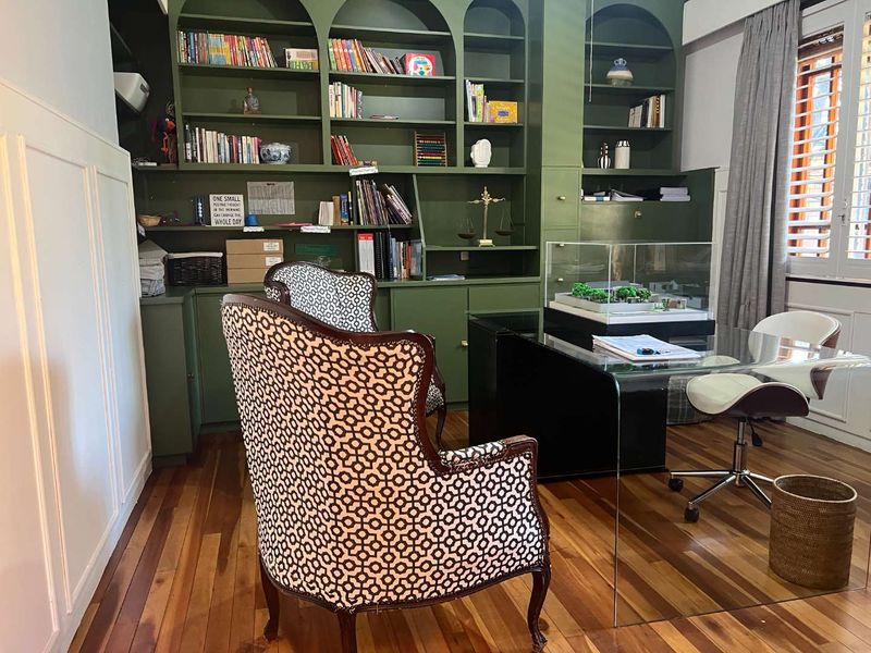 A well-appointed home office featuring extensive built-in floor-to-ceiling shelving, rich hardwood flooring, and classic plantation shutters for adjustable natural light.