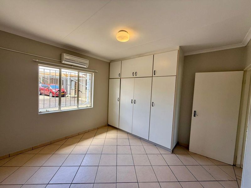 A vacant bedroom featuring tiled flooring, built-in cupboards, and an air conditioning unit, offering a clean and functional space ready for personalization.