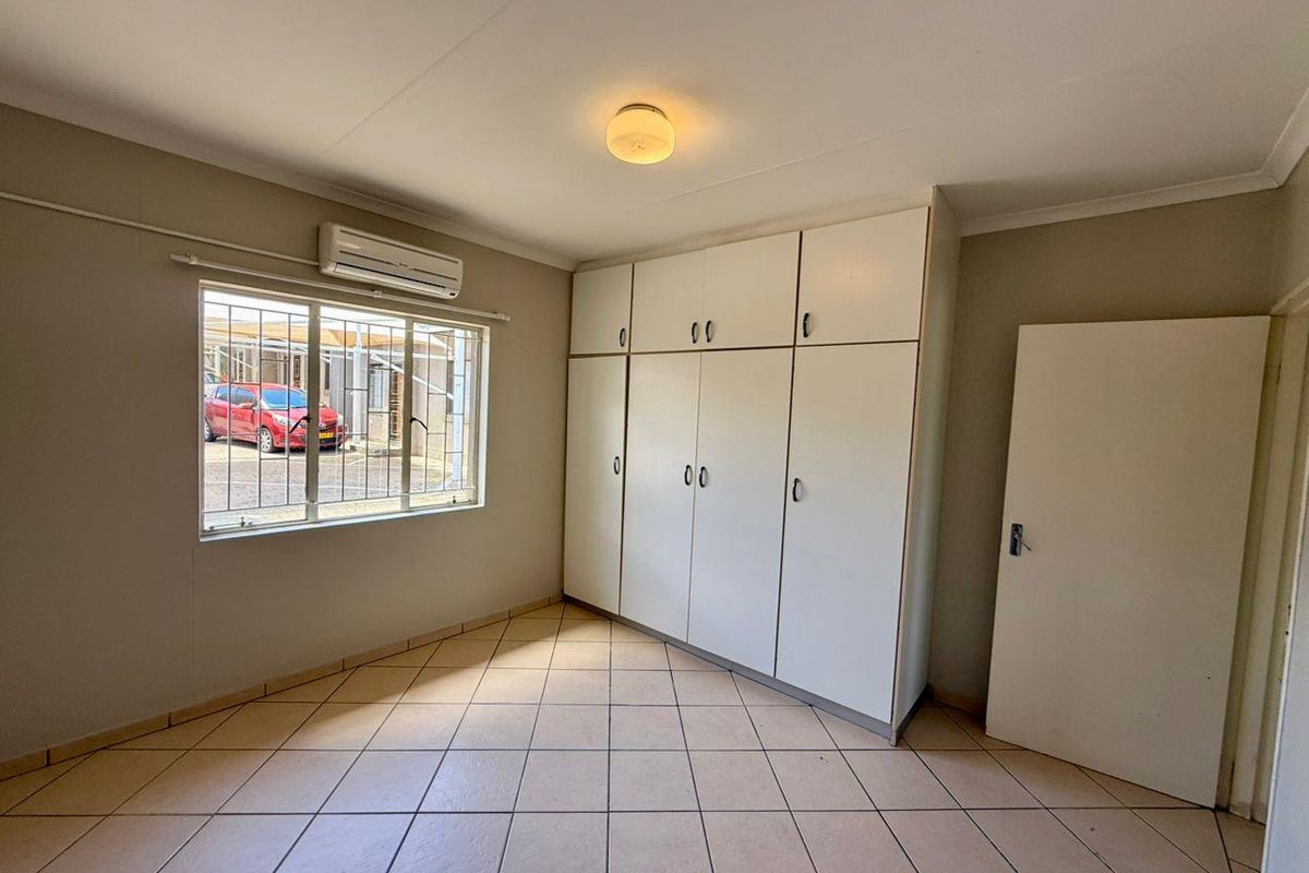 A vacant bedroom featuring tiled flooring, built-in cupboards, and an air conditioning unit, offering a clean and functional space ready for personalization.