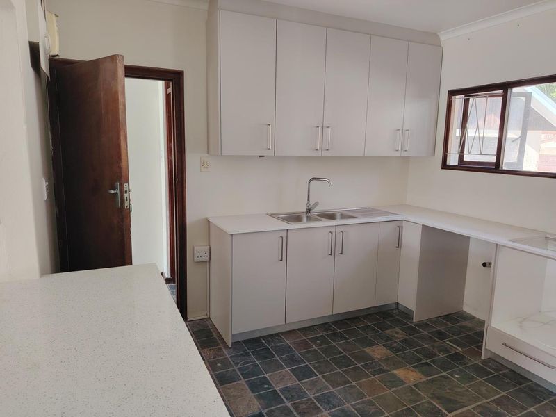 A clean, functional kitchen featuring neutral built-in cabinetry, stone-look countertops, a stainless steel sink, and durable tiled flooring.