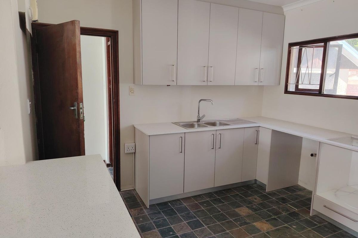 A clean, functional kitchen featuring neutral built-in cabinetry, stone-look countertops, a stainless steel sink, and durable tiled flooring.