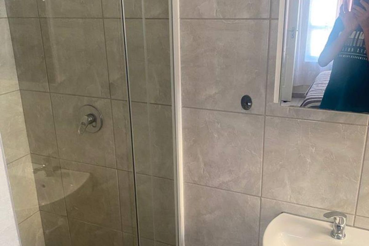 Modern bathroom featuring a glass-enclosed shower with a rainfall showerhead, a wall-mounted mirror, and a pedestal basin with chrome fixtures.