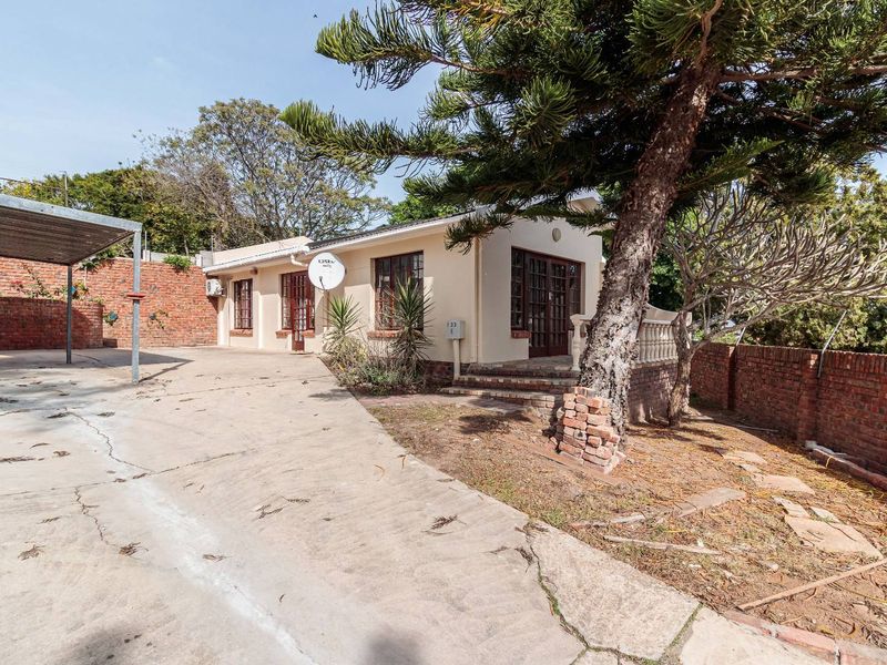 Front exterior view of the property featuring a concrete driveway, carport, and brick boundary walls with established garden elements.