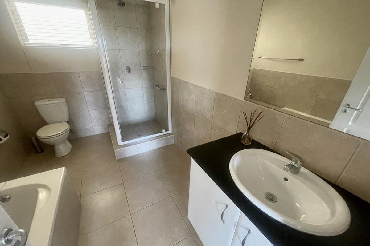 A functional bathroom featuring a glass-enclosed shower, a bathtub, a vanity with a basin, and neutral wall and floor tiling.