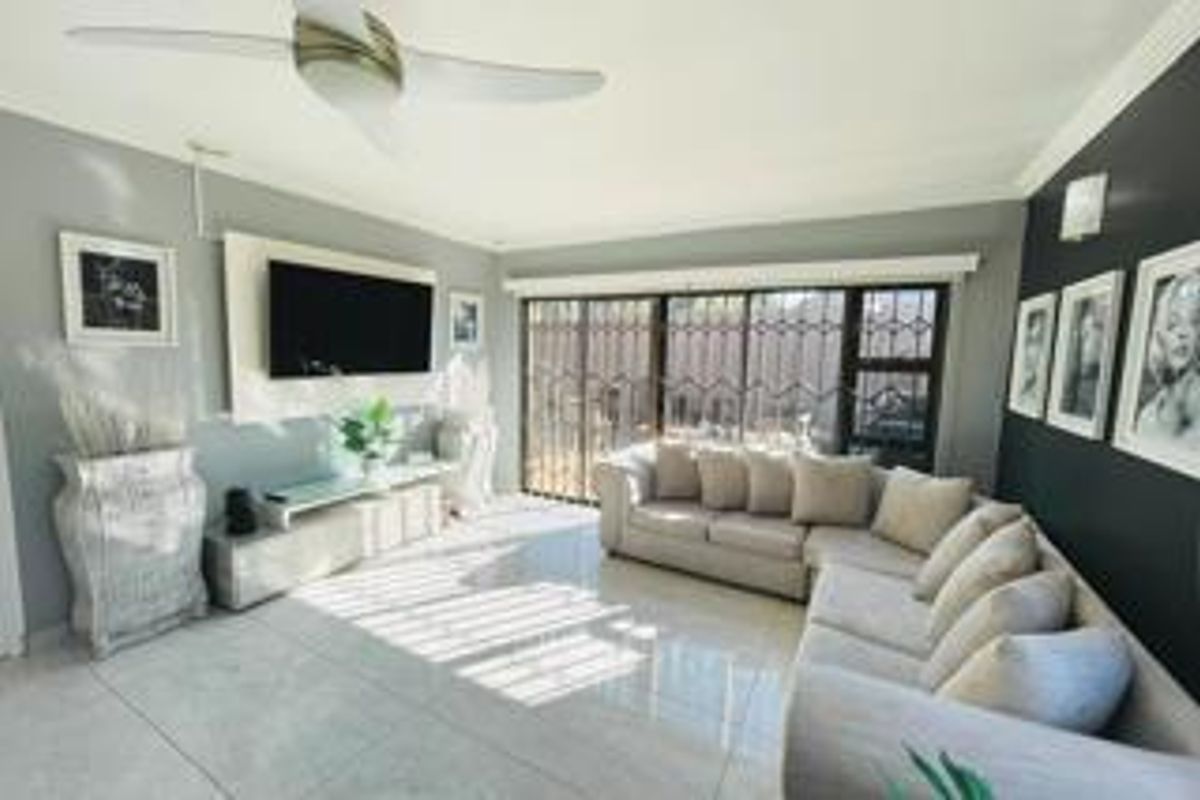 A bright and modern living room featuring large format floor tiles, a ceiling fan, and a sliding glass door with integrated security gate.