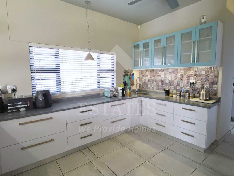 Modern kitchen featuring white base cabinetry, light blue upper cabinets, stone countertops, and a decorative tiled backsplash with ample natural light.