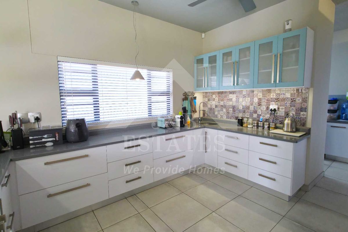 Modern kitchen featuring white base cabinetry, light blue upper cabinets, stone countertops, and a decorative tiled backsplash with ample natural light.