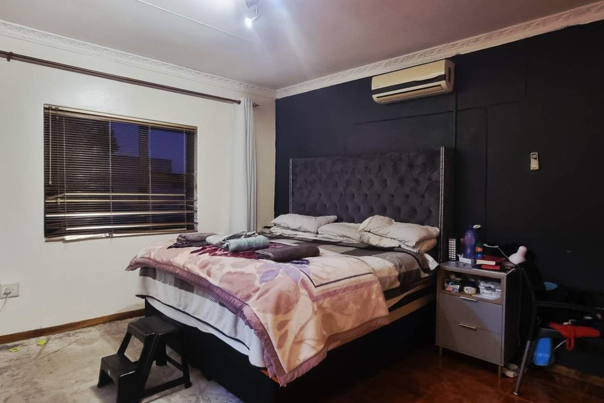 A bedroom featuring an accent wall, air conditioning unit, and venetian blinds, providing a functional space with potential for cosmetic updates.
