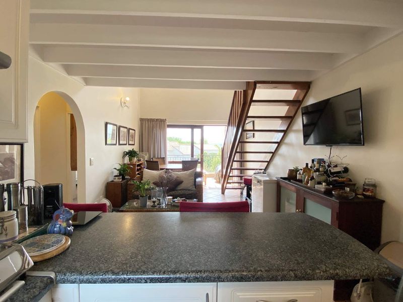 Open plan living area featuring exposed ceiling beams, a wooden staircase, and a kitchen with granite countertops, leading out to a balcony.