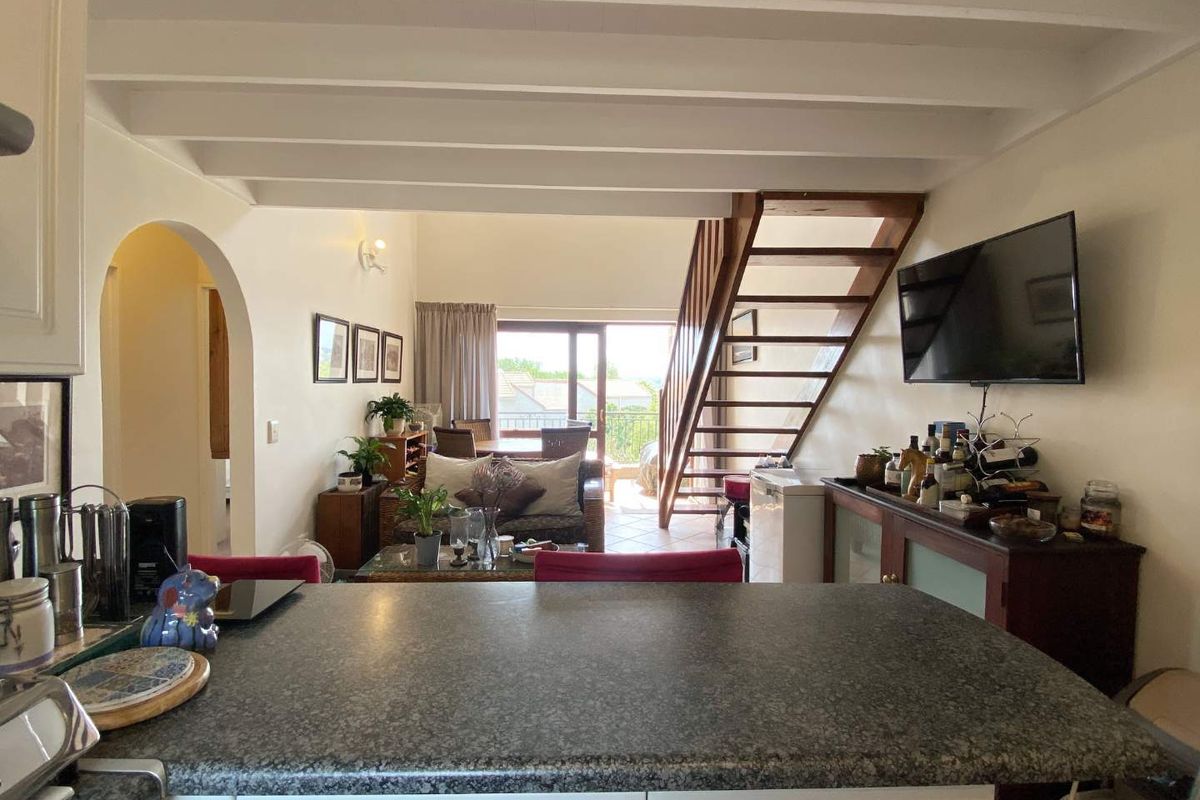 Open plan living area featuring exposed ceiling beams, a wooden staircase, and a kitchen with granite countertops, leading out to a balcony.