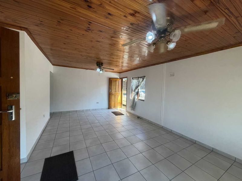 An empty living room featuring ceramic tiled flooring and a timber tongue and groove ceiling with dual ceiling fans.
