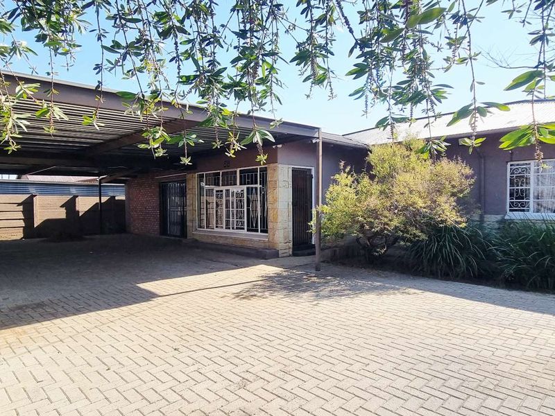 Front exterior view of the property featuring a paved driveway, a large carport, and stone-clad facade details with security bars on windows.