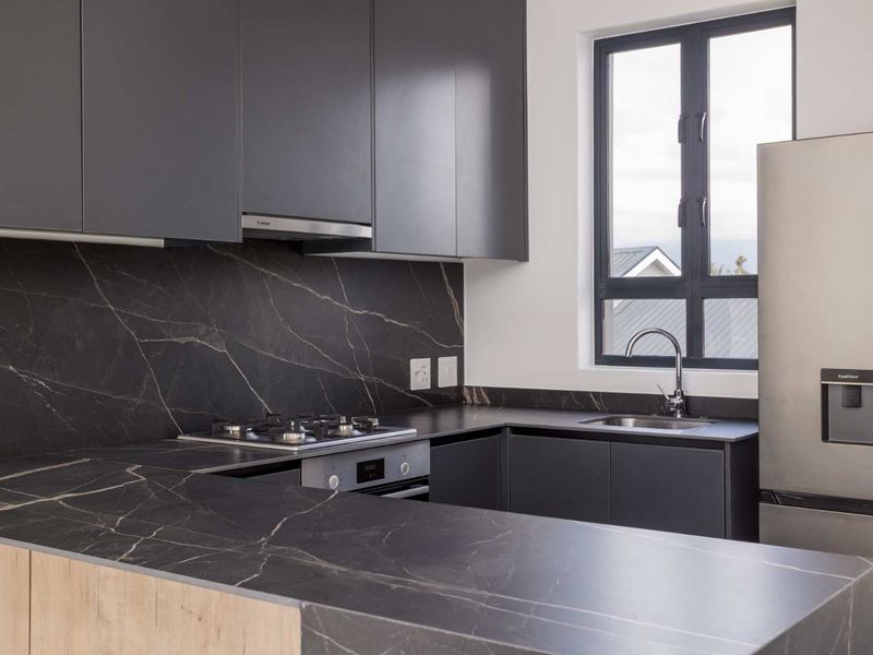 Modern kitchen featuring dark cabinetry, premium stone countertops with matching backsplash, integrated gas hob, oven, and a sleek stainless steel sink.