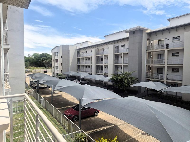 View of the apartment complex exterior featuring paved parking bays with shade cloth carports and multi-story residential building facade.