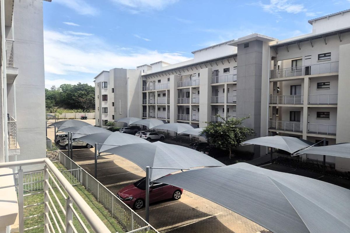 View of the apartment complex exterior featuring paved parking bays with shade cloth carports and multi-story residential building facade.