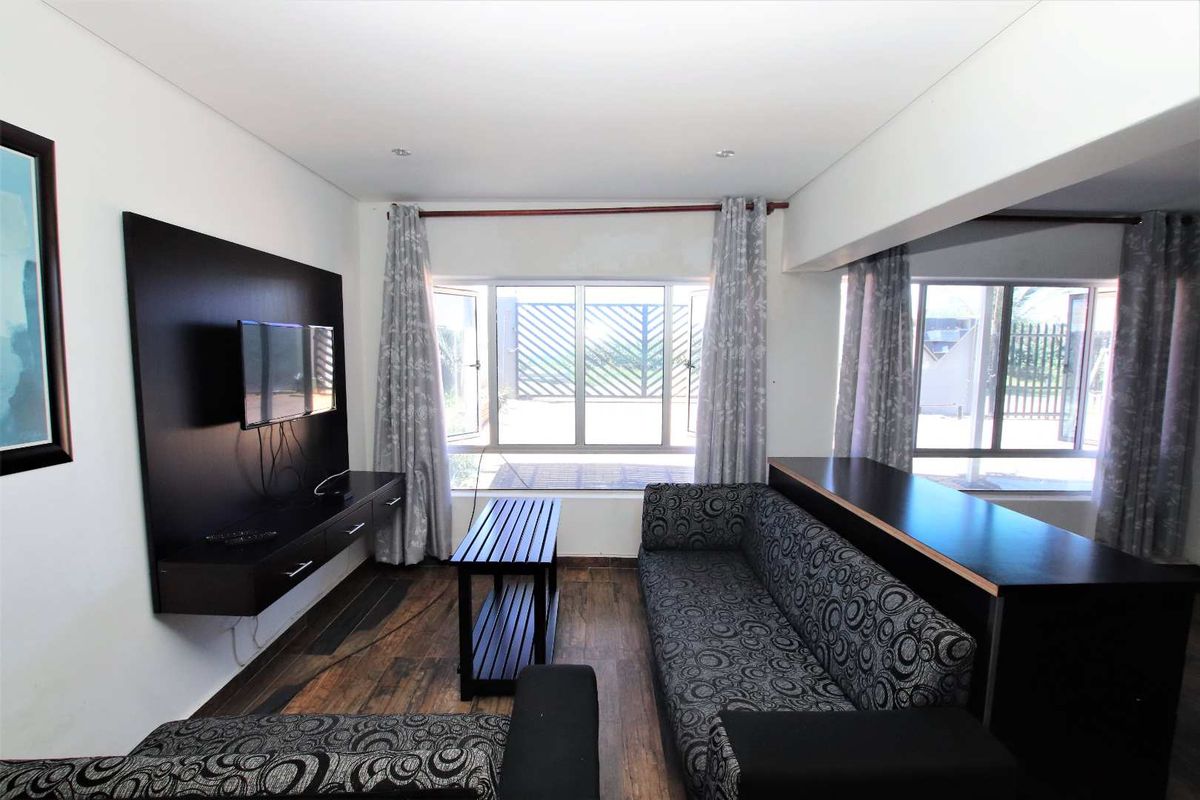 A living room featuring laminate flooring, recessed downlights, and a built-in media console, with large windows providing natural light.