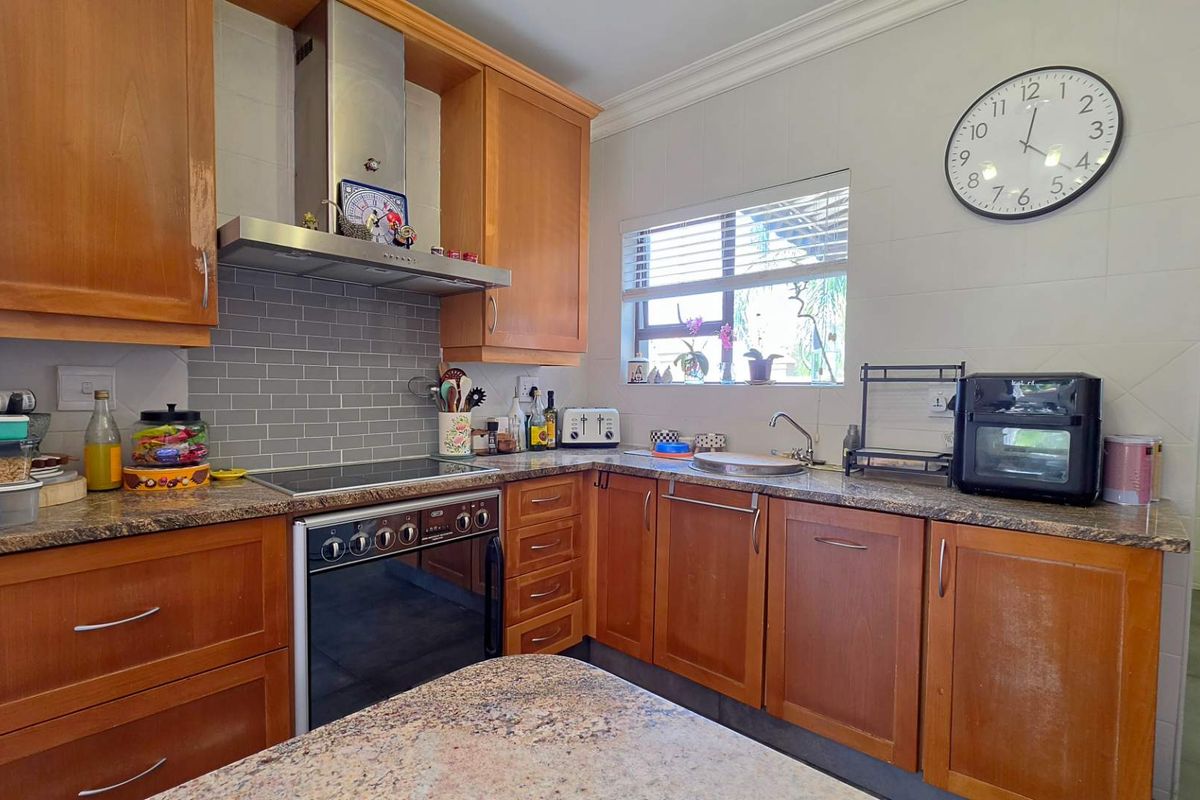 A functional kitchen featuring wooden cabinetry, granite countertops, a subway tile backsplash, and integrated stainless steel appliances including an electric stove and extractor fan.