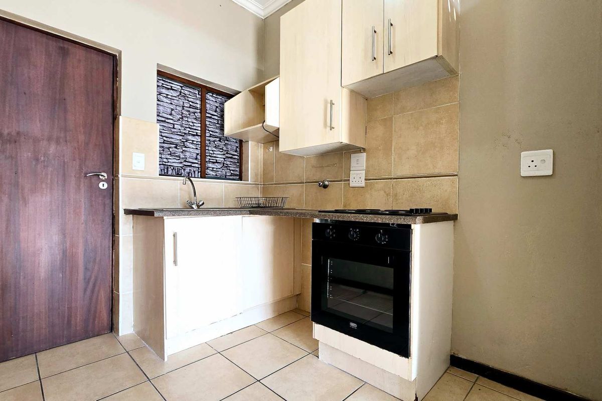 Compact kitchen featuring light-toned cabinetry, tiled backsplash, built-in oven and hob, and tiled flooring.