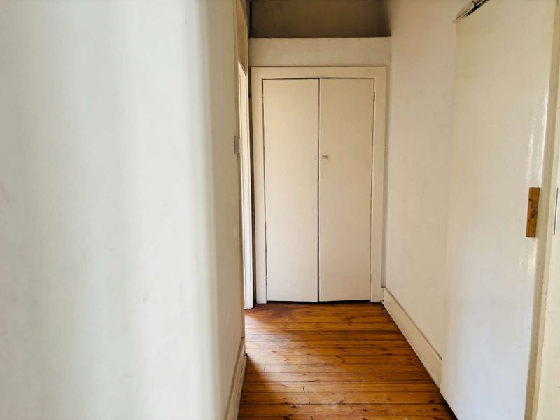 A narrow hallway featuring original timber flooring and a built-in storage cupboard, requiring cosmetic updates to the walls and floor.