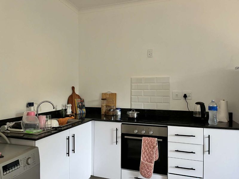 A functional kitchen featuring white cabinetry, black granite countertops, a built-in oven, electric hob, and a subway tile splashback.