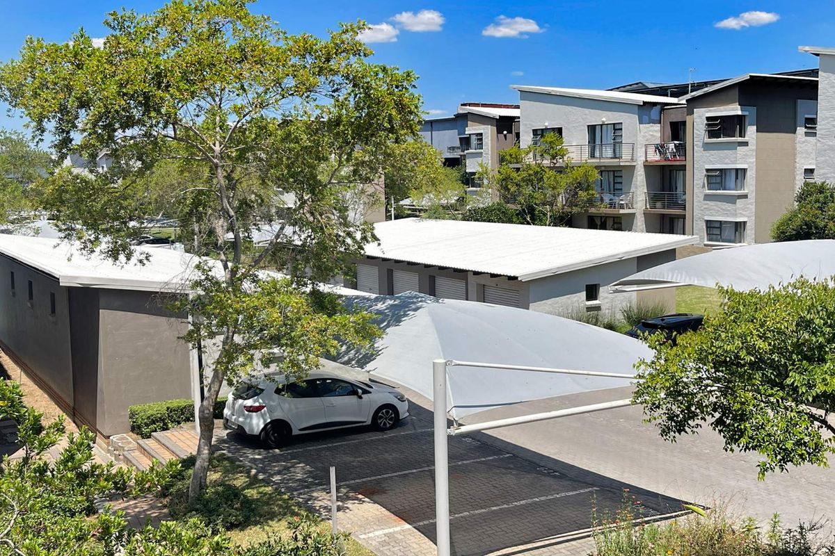 An elevated view of the apartment complex grounds, featuring paved parking areas with shade-cloth carports and modern multi-story residential buildings.