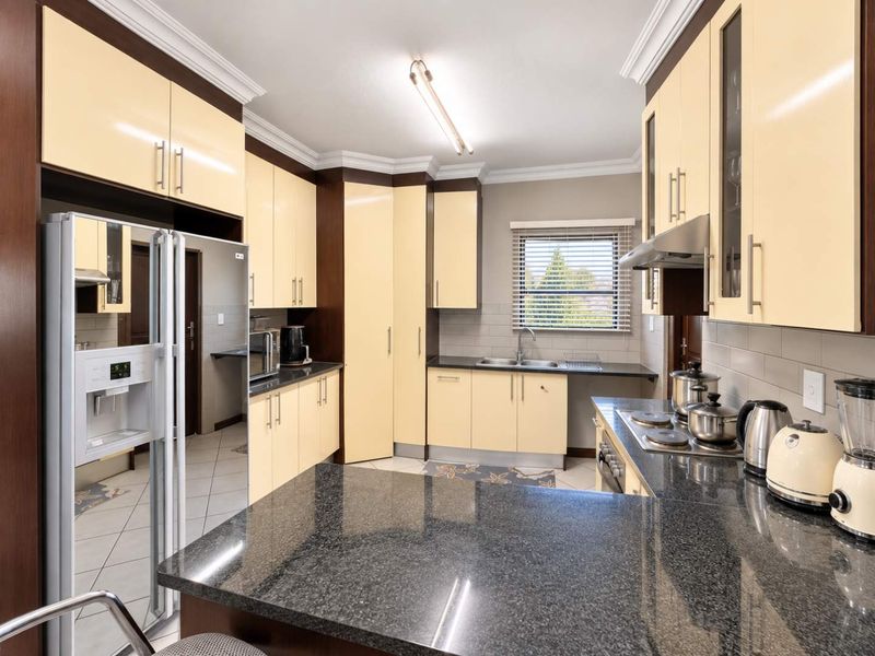 A well-maintained kitchen featuring granite countertops, ample built-in cabinetry, a stainless steel sink, and an integrated electric hob with an extractor fan.