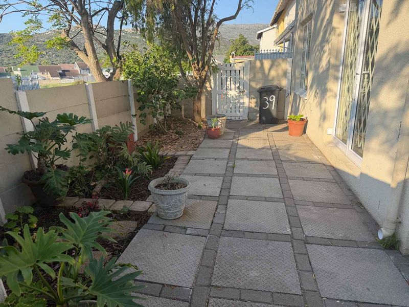 A paved rear courtyard area featuring a precast concrete boundary wall, pedestrian gate, and established garden beds.