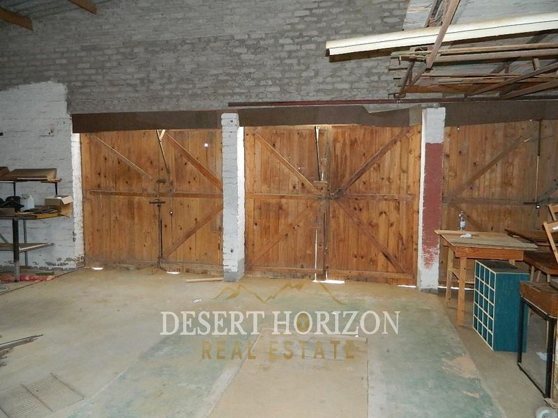 A spacious, unfinished garage area featuring exposed brick walls, concrete flooring, and traditional timber double doors.