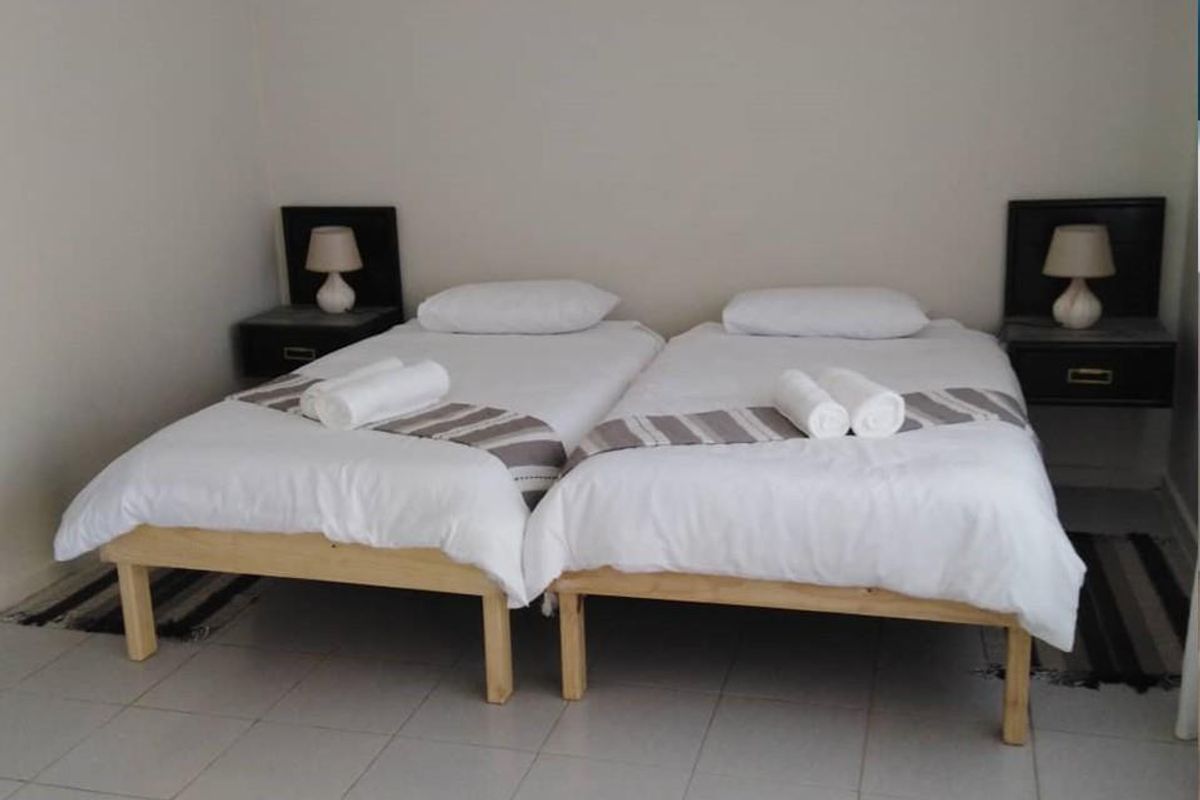 A hotel bedroom featuring twin beds with tiled flooring and wall-mounted bedside shelving units.