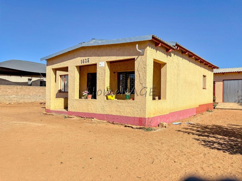 Front view of a single-story detached house featuring plastered masonry walls, security bars on windows, and a corrugated metal roof.