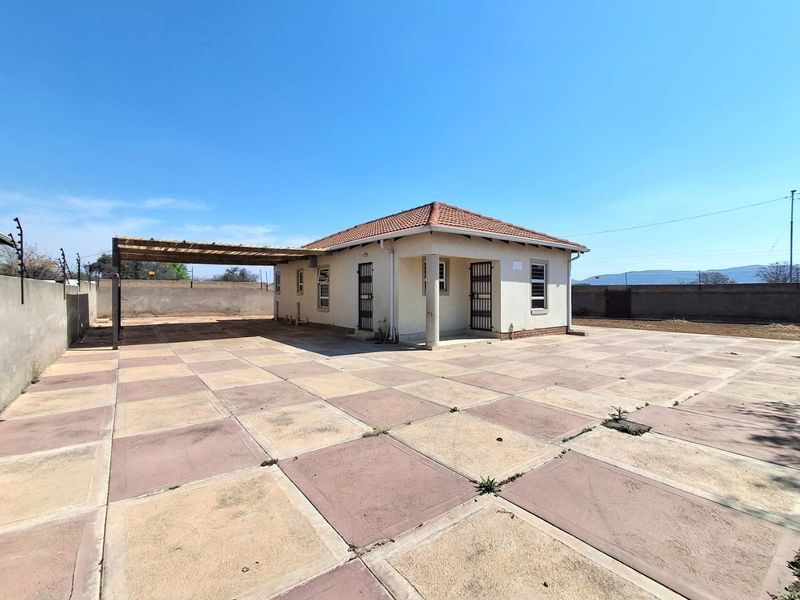 Rear view of the property featuring a large paved courtyard, covered carport, and secure perimeter wall with electric fencing.
