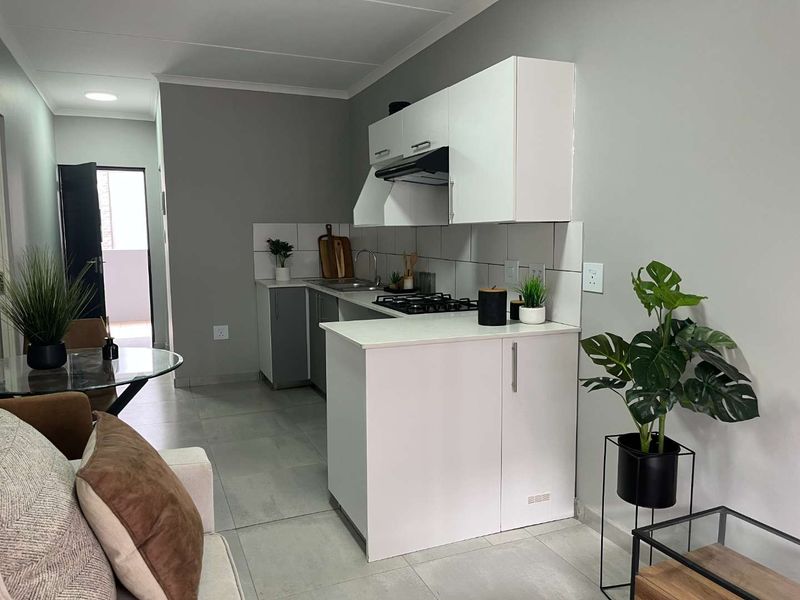 Modern open-plan kitchen featuring white cabinetry, a gas hob with extractor fan, and neutral tiled flooring, seamlessly integrated with the living area.