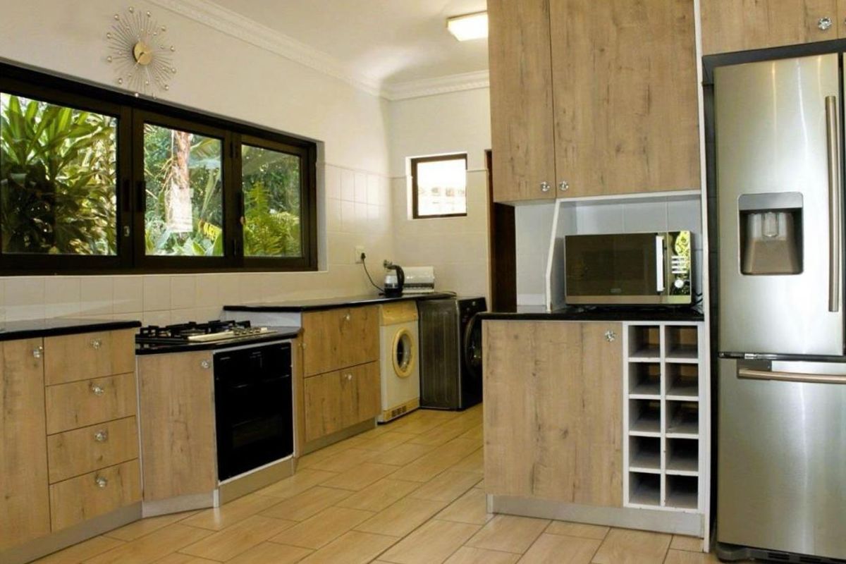 Modern kitchen featuring wood-look cabinetry, black countertops, built-in oven, gas hob, and integrated laundry appliances with tiled flooring.