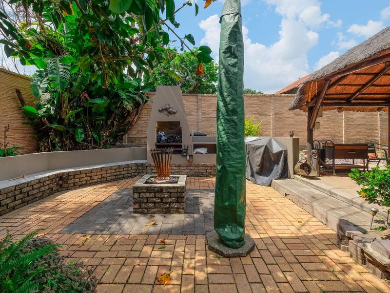 Outdoor entertainment area featuring a built-in braai, brick-paved patio, and a traditional thatched lapa structure.