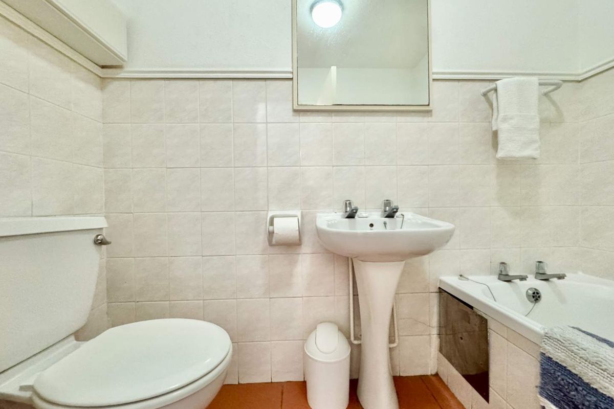 A functional bathroom featuring a pedestal sink, a standard toilet, and a bathtub with tiled walls and flooring.