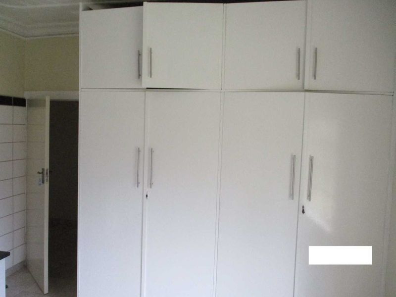 A bedroom featuring white built-in cupboards with overhead storage and tiled flooring.