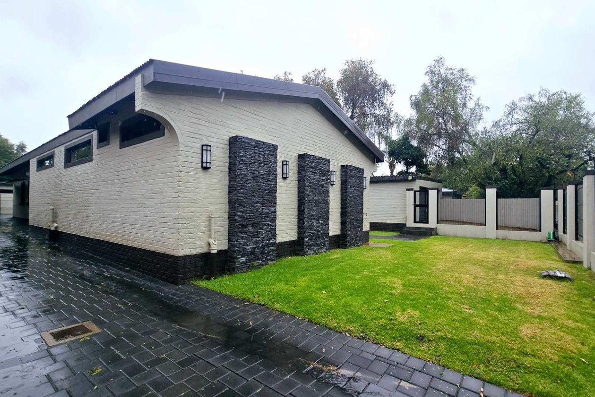 Rear exterior view featuring a paved driveway, landscaped lawn, and a modern facade with stone cladding accents and wall-mounted lighting.